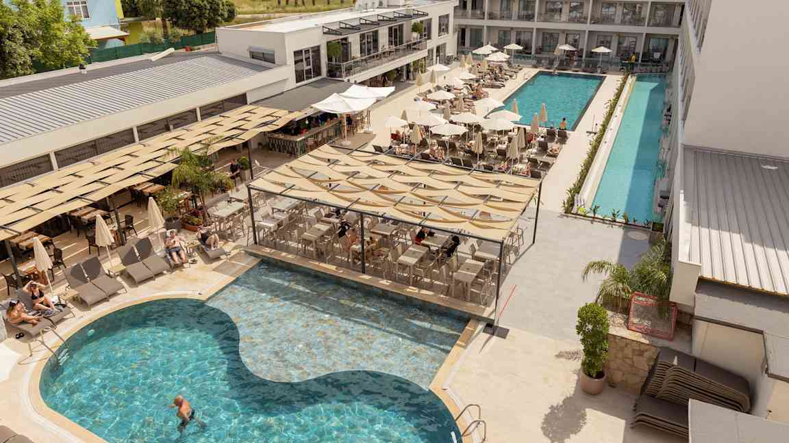 Hotellets poolområde med liggestole, parasoller og servering ved poolen. (AI-genereret tekst)