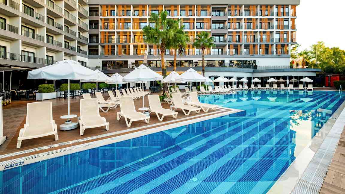 Et hotel ved en pool med liggestole og parasoller. (AI-genereret tekst)