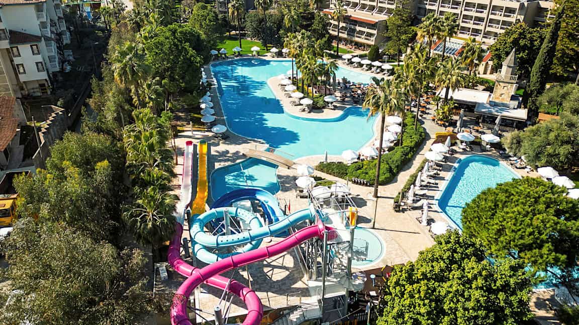 Udsigt over et resort med flere pools og vandrutsjebaner, omgivet af grønne områder. (AI-genereret tekst)