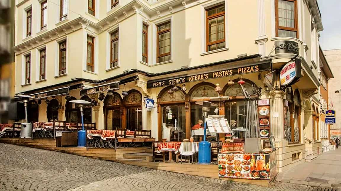 En gade med en bygning med restaurant og udendørs servering, skilte med mad som kebab og pizza. (AI-genereret tekst)