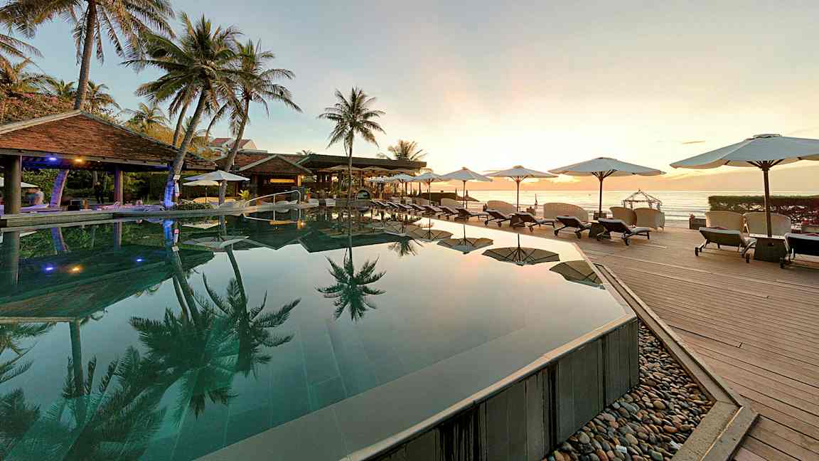 En pool med udsigt over havet omgivet af palmer og liggestole. (AI-genereret tekst)