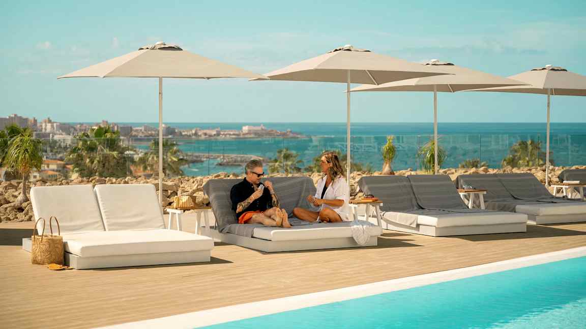 Liggestole og parasoller ved en pool med udsigt over havet. (AI-genereret tekst)