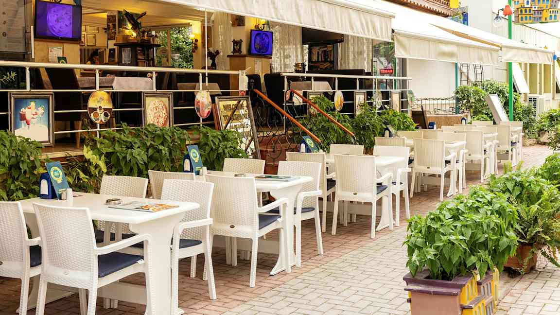 Restaurant med udendørs servering med hvide borde og stole ved et hotel. (AI-genereret tekst)