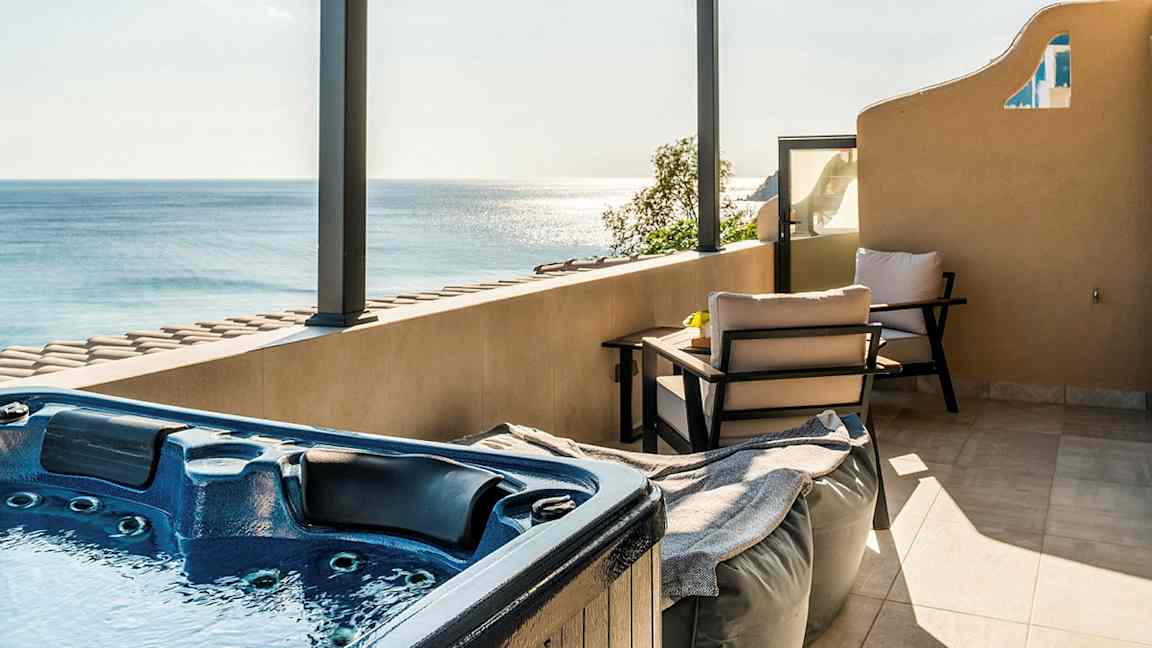 En terrasse med jacuzzi, siddepladser og udsigt over havet under en tagpergola. (AI-genereret tekst)