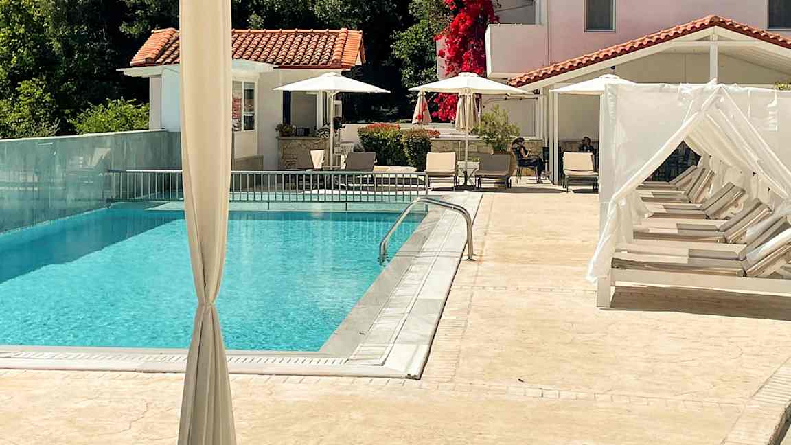 En udendørs swimmingpool med liggestole og et hvidkalket hus i baggrunden. (AI-genereret tekst)