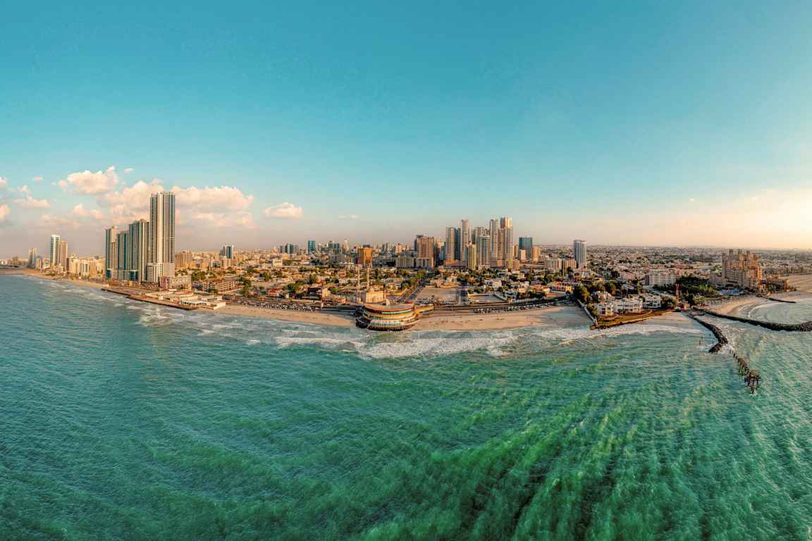 Panoramabillede af en kystby med højhuse, strand og hav. (AI-genereret tekst)