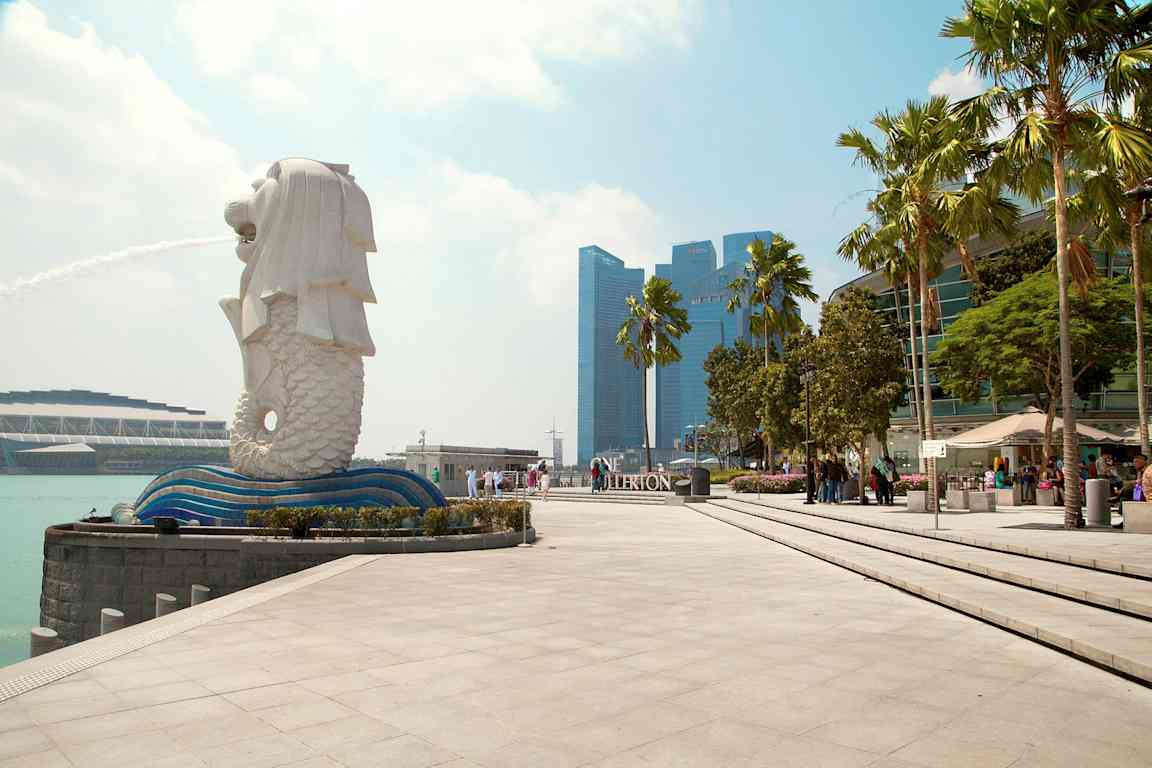 Billede af Merlion-statuen i Singapore med fontæne, omgivet af moderne arkitektur og palmer. (AI-genereret tekst)