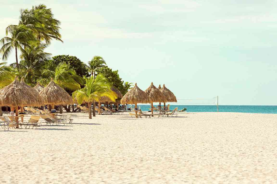 En strand med parasoller lavet af palmeblade, liggestole og et net til strandvolleyball. (AI-genereret tekst)