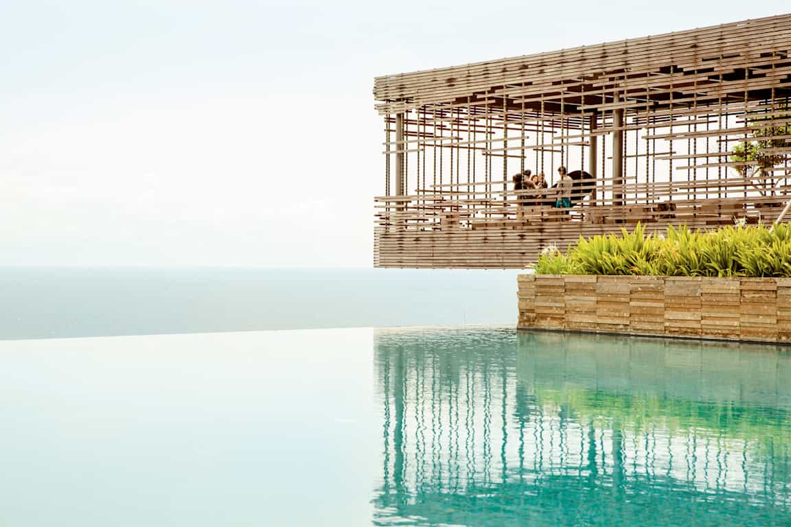 Udsigt over en infinitypool med havet i baggrunden og en træpavillon, der svæver ved kanten. (AI-genereret tekst)