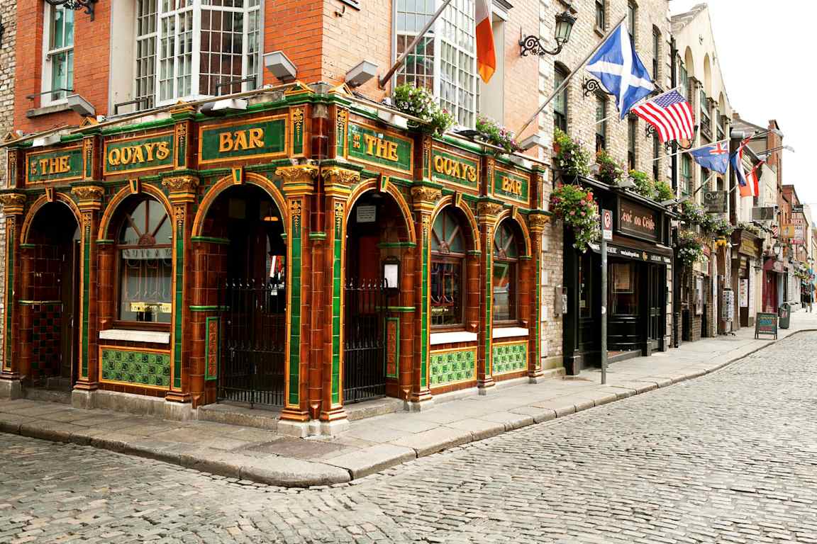 En farverig pub med grøn og orange dekoration i traditionel stil ligger ved en brostensbelagt gade. (AI-genereret tekst)