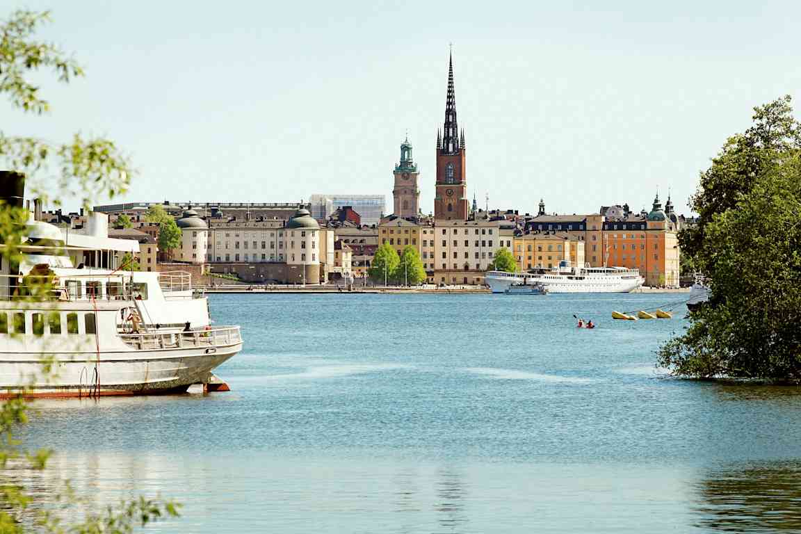 En byudsigt med bygninger, vand og en kirke med et højt spir, set fra et sted ved vandet. (AI-genereret tekst)