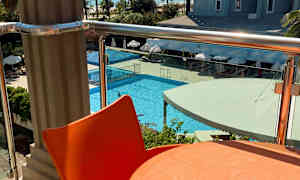 Udsigt fra en balkon med et orange bord og stol i forgrunden, en pool og et hotel i baggrunden. (AI-genereret tekst)