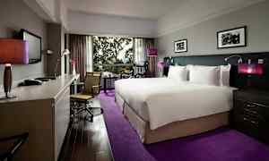 Hotelværelse med en stor seng og moderne indretning, skrivebord og stol samt en udsigt gennem et stort vindue. (AI-genereret tekst)