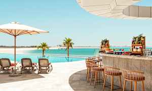 En pool ved stranden med liggestole, parasol og en poolbar med eksotiske frugter. (AI-genereret tekst)