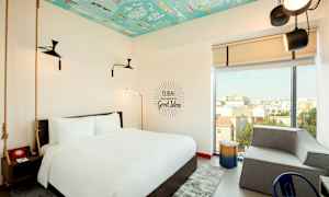 Et hotelværelse med en stor seng, moderne indretning og et farverigt loft. Et stort vindue giver udsigt til byen. (AI-genereret tekst)