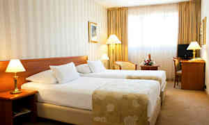 Et hotelværelse med to enkeltsenge, lamper ved siden af sengene og et skrivebord med stol. (AI-genereret tekst)