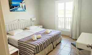 Et hotelværelse med to enkeltsenge, dekoreret med stribet sengetæpper og håndklæder. Et vindue og et skrivebordshjørne er synligt. (AI-genereret tekst)