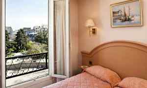 Et hotelværelse med en seng og en åben balkondør, der viser udsigt over en by og et grønt område. (AI-genereret tekst)