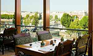 En restaurant med borde og stole tæt på et stort vindue med udsigt over byen og floden. (AI-genereret tekst)