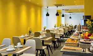 Et moderne restaurantområde med gule vægge, opdækkede borde og en buffet med forskellige madvarer. (AI-genereret tekst)