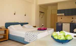 Værelset har en seng med blåt hovedgærde, et køkken og et bord med frugt. (AI-genereret tekst)