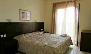 Et hotelværelse med en dobbeltseng, natbord og en åben altandør. (AI-genereret tekst)