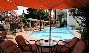 En udendørs pool med liggestole og parasoller omkring samt siddegruppe i forgrunden. (AI-genereret tekst)