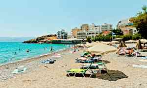 En solrig strand med parasoller, mennesker der bader og bygninger ved stranden. (AI-genereret tekst)