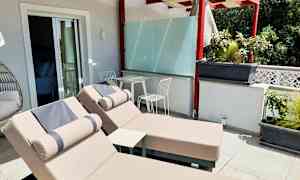 Terrasse med to solsenge og et bord med to stole under en pergola. (AI-genereret tekst)