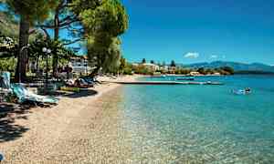 En strand med klart vand, liggestole og træer. (AI-genereret tekst)