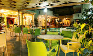 En udendørs lounge med borde og stole ved siden af en pool, oplyst om aftenen. (AI-genereret tekst)