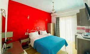 Et hotelværelse med en dobbeltseng, rødt vægparti og lyseblåt sengetæppe. (AI-genereret tekst)