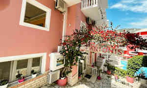 En lyserød bygning med hvide vinduer, skilt med teksten 'Antonis' og røde blomster. (AI-genereret tekst)