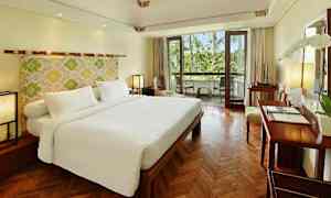 Et hotelværelse med en stor dobbeltseng, trægulv og en balkon med udsigt til grøntområder. (AI-genereret tekst)