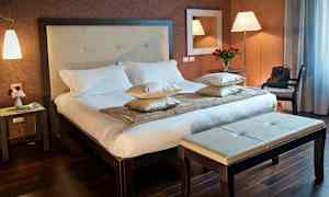 Et hotelværelse med en dobbeltseng, sidebord og bænk. (AI-genereret tekst)