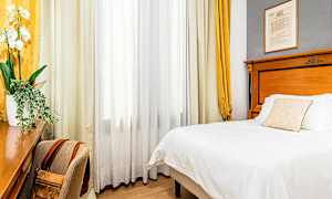 Et hotelværelse med en seng, et skrivebord og en stol. Gardiner hænger ved et vindue. (AI-genereret tekst)