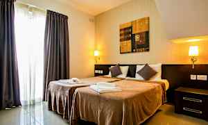 Et hotelværelse med to enkeltsenge, natbord, væglamper, et maleri over sengene og gardiner ved et vindue. (AI-genereret tekst)