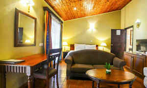 Et værelse med seng, sofa, bord, skrivebord og dekorationer. (AI-genereret tekst)