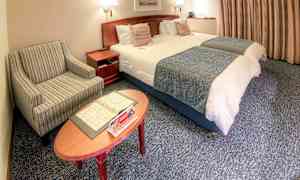 Et hotelværelse med to redte enkeltsenge, en stribet lænestol og et sofabord med brochurer. (AI-genereret tekst)