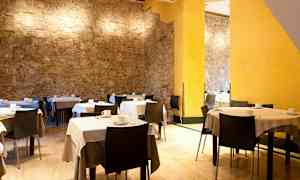 Et rum med borde og stole, hvide duge og kaffekopper samt stenvægge og gule vægdetaljer. (AI-genereret tekst)