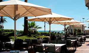 Udendørs restaurantområde med borde, stole og parasoller tæt på havet. (AI-genereret tekst)