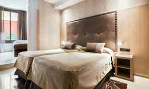 Et hotelværelse med to enkeltsenge ved siden af hinanden og en sengegavl i mørkt materiale. Der er et lille natbord og en stor vinduesflade, der lukker naturligt lys ind. (AI-genereret tekst)