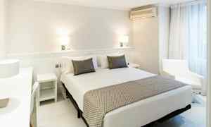 Et lyst og moderne hotelværelse med en bred seng, to natborde og en lænestol ved vinduet. (AI-genereret tekst)