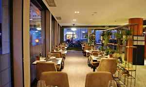 En hyggelig restaurant med borde og stole arrangeret langs vinduer og et dekorativt stativ med planter. (AI-genereret tekst)