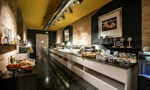 Buffetområde med mad og drikkevarer på flere borde, omgivet af murstensvægge og moderne belysning. (AI-genereret tekst)