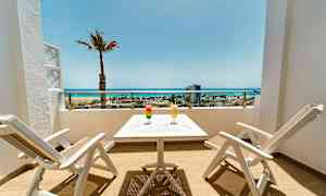 Terrasse med to hvide stole og et bord, to drikkevarer og udsigt over stranden og havet. (AI-genereret tekst)