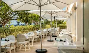 En udendørsterrasse med hvide borde og stole samt hvide parasoller. (AI-genereret tekst)