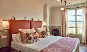 Et hotelværelse med en seng, dekorative puder og et vindue med udsigt. (AI-genereret tekst)