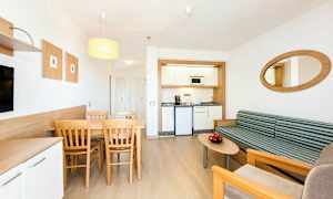 Et moderne hotelværelse med en lille køkkenkrog, en spiseplads med bord og stole samt en siddegruppe med sofa og sofabord. (AI-genereret tekst)