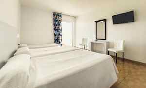 Et hotelværelse med tre enkeltsenge, et skrivebord med spejl, to stole og et vægmonteret TV. (AI-genereret tekst)